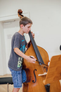 Junge in grauem T-shirt und blauen Shorts spielt Kontrabass